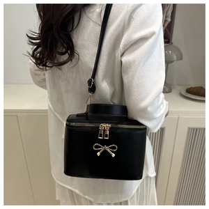Detail of a chic black box bag with golden bow ornament worn over the shoulder