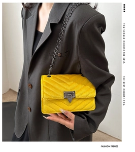 Close-up of bright yellow quilted velvet crossbody bag with V-shaped stitching and chain