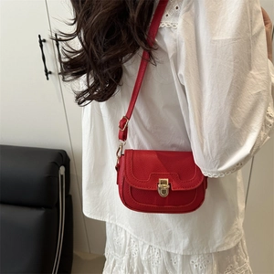 Red pebbled leather crossbody bag with gold buckle worn by model in casual setting