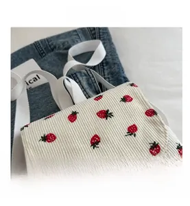 Detail of white corduroy tote bag featuring red strawberry print and cotton strap