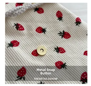 Detail of white corduroy bag showing strawberry print and gold magnetic buckle