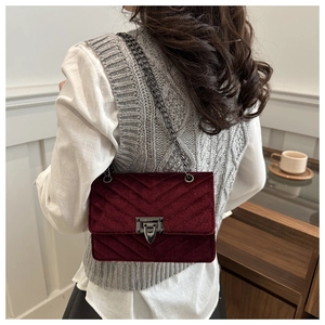 Detail of burgundy velvet chevron quilted bag with dark metal chain strap on model