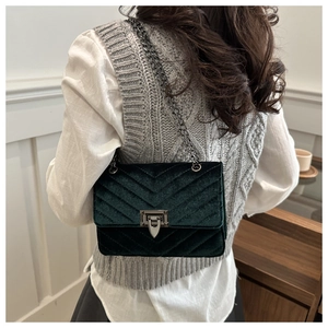 Detail of dark green velvet crossbody bag featuring herringbone quilting and chain strap