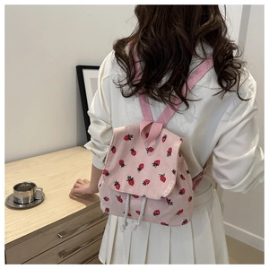 Pink corduroy mini backpack featuring strawberry prints on a model in a cozy setting