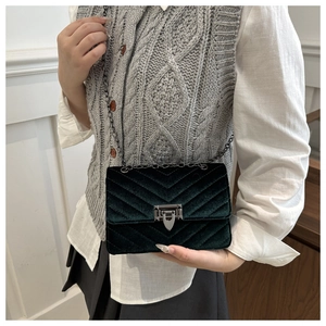 Detail of dark green velvet crossbody bag with V-shaped quilting and metal chain strap