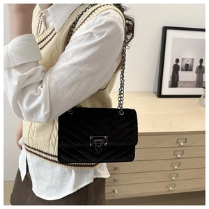 Detail of black velvet crossbody bag with V-shaped quilting and metallic chain strap