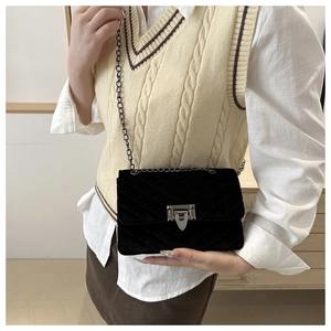 Detail of black velvet quilted crossbody bag featuring silver chain and metal turn-lock