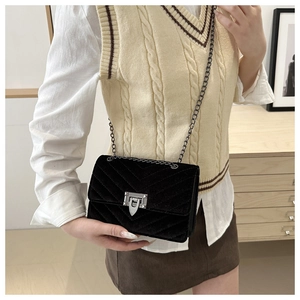 Detail of a black quilted velvet crossbody bag with silver buckle and metal chain