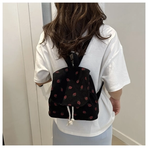 Detail of black corduroy mini backpack with red strawberry print shown on model back