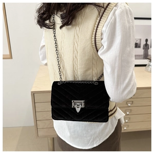 Rear view of model wearing a black velvet quilted crossbody bag with silver chain strap