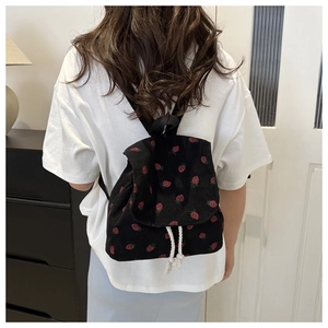 Detail of strawberry print black corduroy backpack showing white drawstring on model