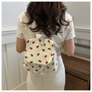 Detailed texture of white corduroy backpack featuring red strawberry print and drawstring