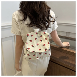 Detailed view of white corduroy backpack featuring red strawberry pattern and drawstrings