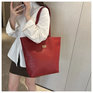 Macro shot of red faux crocodile leather texture and gold metal plate detail on tote bag