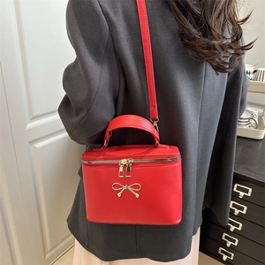 Elegant red square crossbody box bag with gold bow clasp worn with a grey blazer