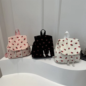 Three corduroy strawberry print backpacks in pink, black and white on a white stand