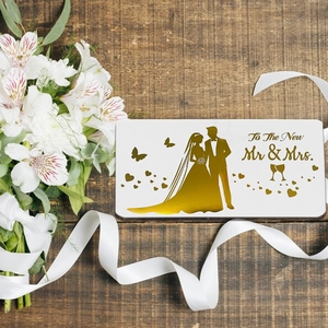 Elegant white wedding card with gold foil silhouette on a dark wood table with flowers