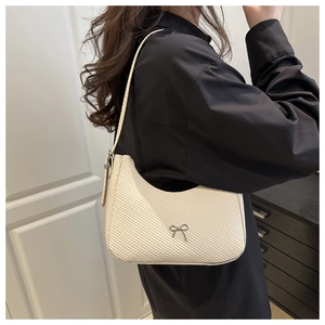 Detail view of off-white woven hobo bag with a silver bow ornament on a black shirt