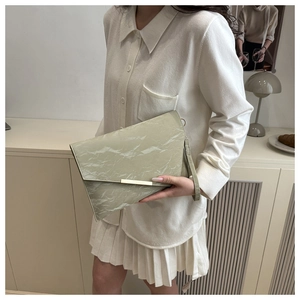 Détail d'une pochette enveloppe marbre vert clair avec boucle dorée et dragonne assortie