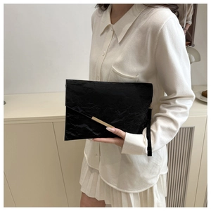 Détail de la pochette enveloppe noire plissée avec barre dorée et dragonne au poignet