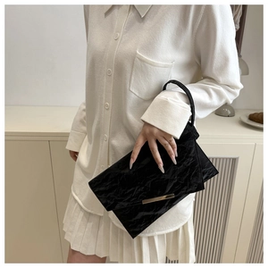 Détail d'une pochette enveloppe plissée noire avec garniture dorée portée par un mannequin