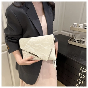 Détail d'une pochette enveloppe plissée beige avec garniture métallique et dragonne élégante