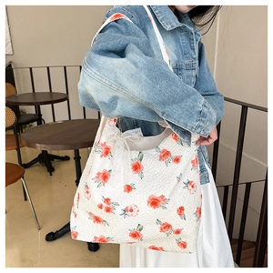 Detail of floral tote bag featuring red rose patterns, white lace bow, and pearl chain