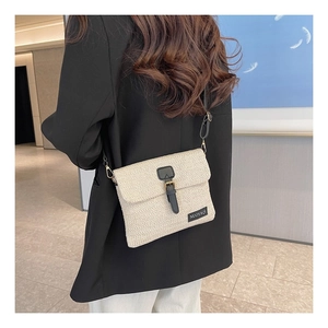 Detail of woven straw crossbody bag with black leather strap on a model with black blazer