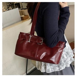 Dettaglio borsa sottobraccio in pelle lucida bordeaux con fibbia decorativa e tracolla larga