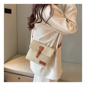 Detail of woven straw crossbody bag with brown leather strap and decorative buckle flap