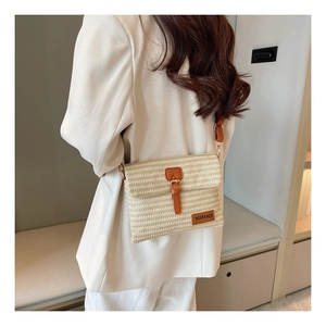 Detail of a beige woven straw crossbody bag with brown leather strap and buckle on a model