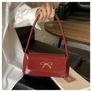 Détail du sac baguette rouge foncé brillant avec boucle nœud doré et fine bandoulière