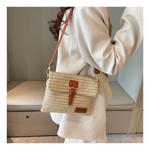 Detailed close-up of woven straw texture and brown leather buckle on a crossbody bag