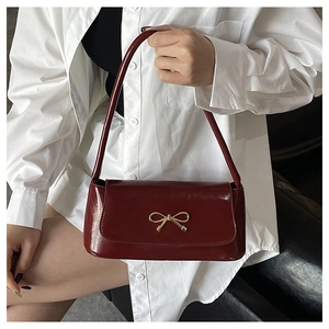 Détail du sac baguette en cuir brillant bordeaux avec une boucle nœud dorée