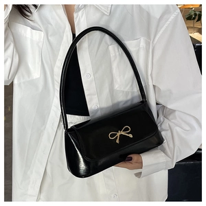 Détail du sac baguette noir brillant avec une boucle métallique en nœud doré sur la bandoulière