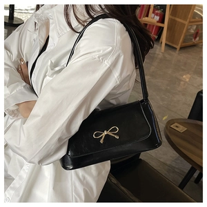 Détail du sac baguette noir avec nœud doré porté sur une chemise blanche élégante