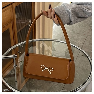 Détail macro du sac porté épaule en cuir verni caramel avec boucle nœud dorée