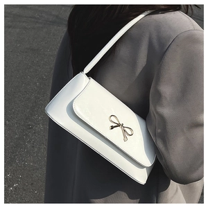 Sac baguette en cuir blanc avec boucle nœud doré porté à l'épaule par un mannequin