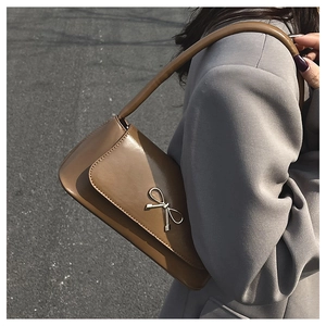 Détail d'un sac baguette marron avec boucle nœud argenté sur un blazer gris
