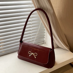 Détail du sac baguette en cuir plissé bordeaux avec un nœud doré et un rabat chic