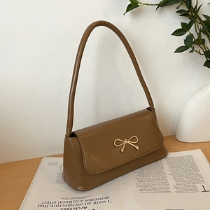 Détail du sac baguette en cuir PU marron caramel avec boucle noeud dorée sur bois