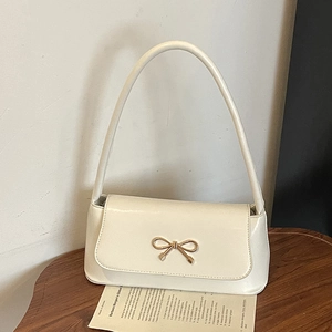 Sac baguette élégant blanc crème avec fermoir nœud doré sur une table en bois