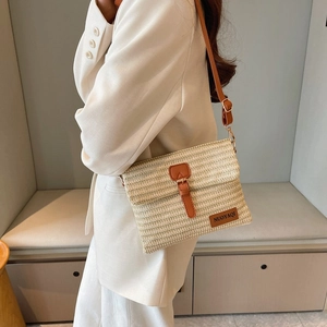 Woven straw messenger bag with brown leather trim and metal buckle on white blazer