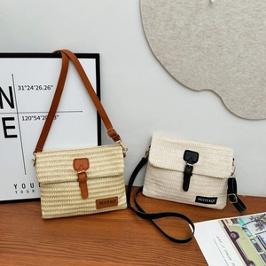 Handwoven straw crossbody beach bag with leather strap and flap closure on wood desk