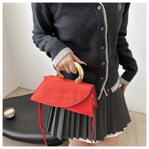 Detail of red square bag featuring a unique gold sculpted handle and asymmetric flap design