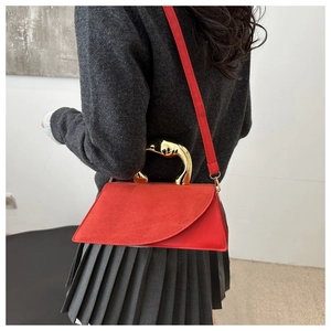 Detail of red crossbody bag with asymmetrical suede flap and gold metal handle