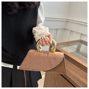 Detail of brown suede handbag featuring a unique gold U-shaped metal handle and strap