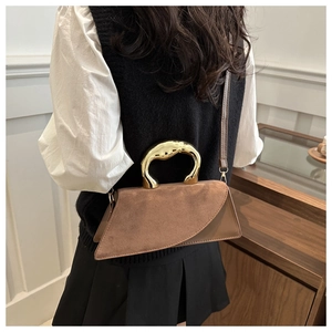 Detail of brown suede handbag with sculptural gold metal handle worn over the shoulder
