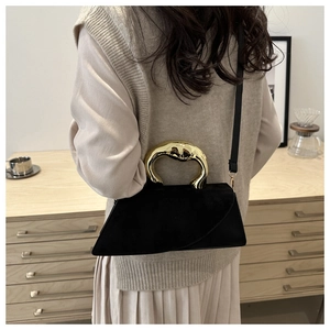 Detail of artistic gold metal handle on a black suede handbag worn by a model