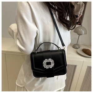 Detailed view of black pebbled leather handbag with sparkling rhinestone buckle on a model